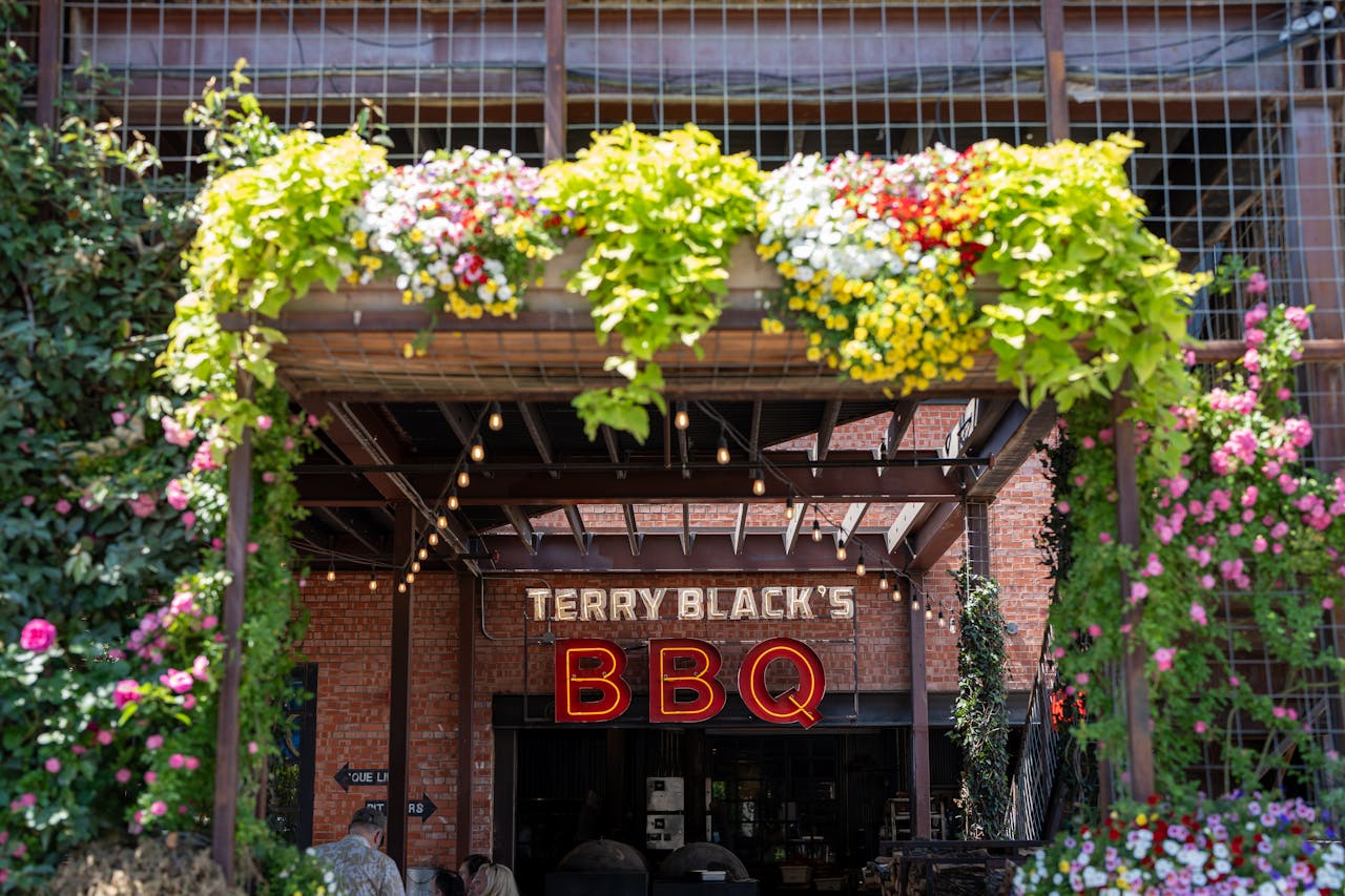 Entrance of Terry Blacks BBQ with vibrant flowers in Dallas, Texas.