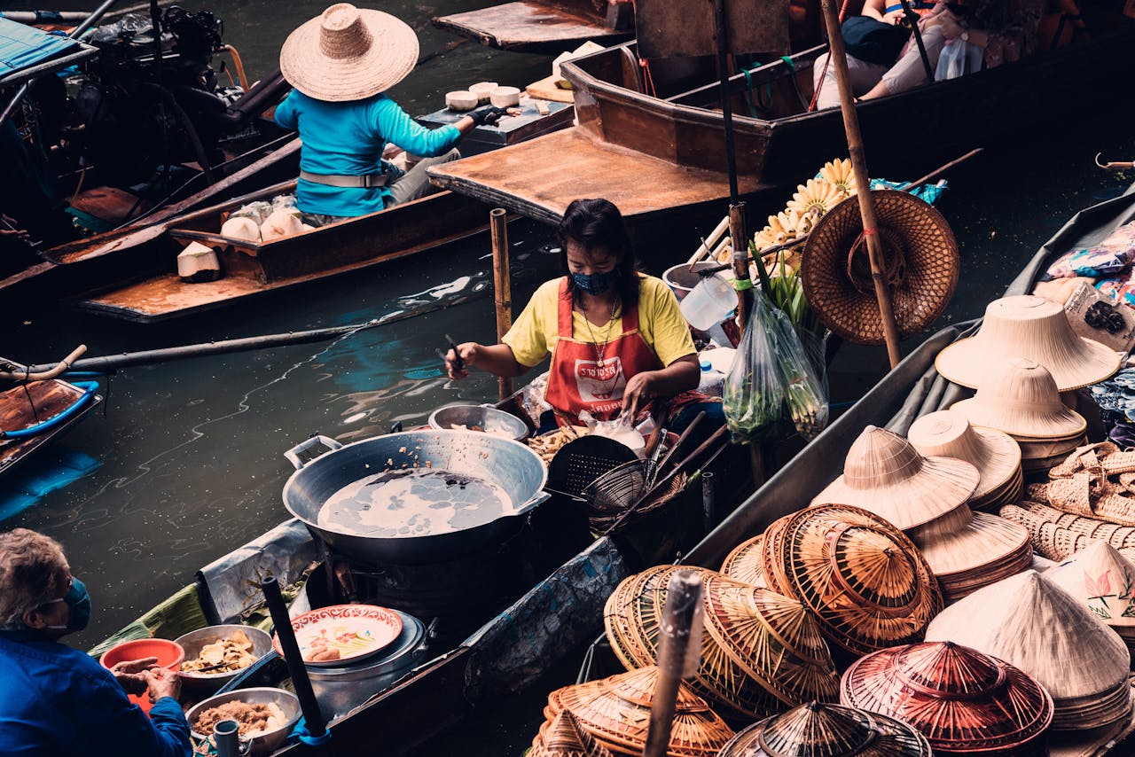 Traditional floating market in Bangkok featuring vendors selling hats and food from boats.